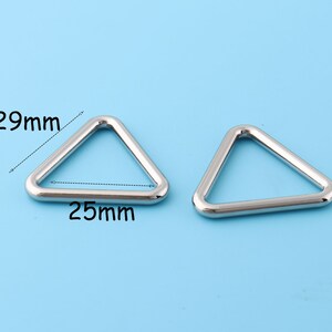 Op de afbeelding: Twee zilveren driehoekige metalen ringen. De ringen meten 29 mm bij 25 mm.