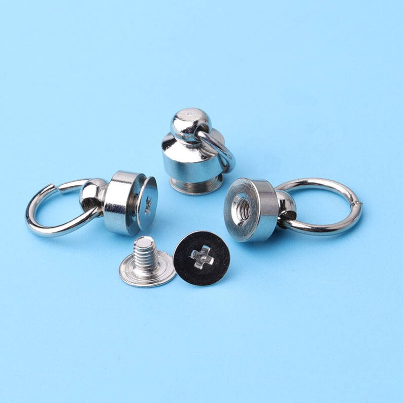 May include: Four silver metal snap fasteners with a loop and a screw. The fasteners are used for attaching fabric or leather together.