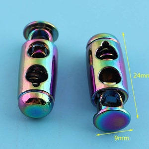 Puede incluir: Dos topes de cordón de metal iridiscente con un mecanismo de resorte. Cada tope mide 24 mm de largo y 9 mm de diámetro.