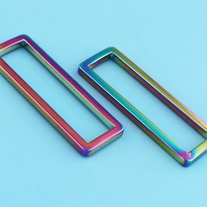 May include: Two iridescent metal rectangular rings, one slightly larger than the other, on a light blue background.