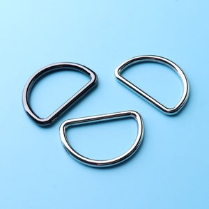 May include: Three metal D-rings, two silver and one black, on a light blue background.