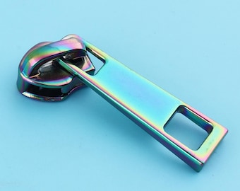 May include: A iridescent zipper pull with a rectangular slider and a rounded top. The pull is made of metal and has a rainbow finish.