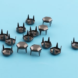May include: A collection of 15 black metal hexagonal studs with pointed tips. The studs are scattered on a light blue background.