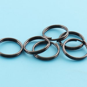 May include: Six black metal key rings, each with a double loop, are arranged on a light blue background.