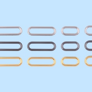 May include: A set of 12 oval-shaped metal rings in three different finishes: silver, black, and gold. The rings are all the same size and shape, and they are arranged in three rows of four.