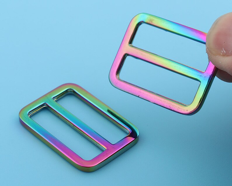 May include: Two iridescent rainbow-colored metal slider buckles. The buckles are rectangular with a single horizontal slot in the center.