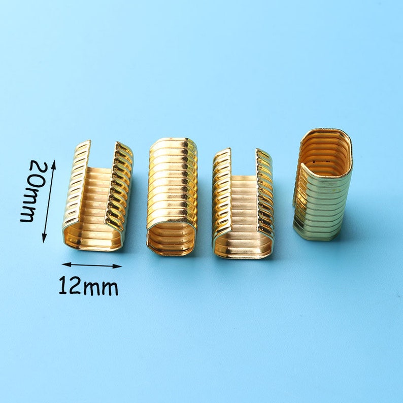 May include: Four gold-colored metal clasps, each measuring 12 mm wide and 20 mm long. The clasps have a ribbed design and are ideal for attaching to fabric or other materials.