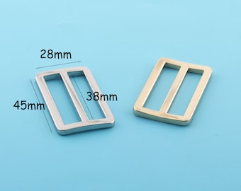 Könnte beinhalten: Zwei Metall-Schieber-Schnallen, eine silberne und eine goldene. Die silberne Schnalle misst 45 mm x 38 mm und 28 mm breit. Die goldene Schnalle ist gleich groß.