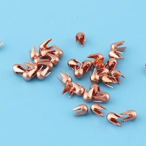 May include: A group of 20 rose gold metal nail heads with a pointed tip and a decorative crown design.