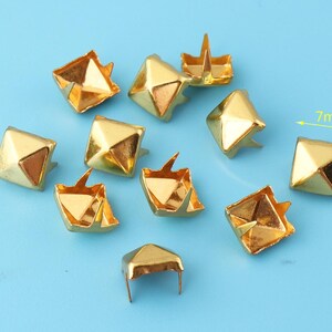 May include: Ten gold-colored metal pyramid studs, each measuring 7mm in size. The studs have a square base and a pointed top. They are ideal for adding a decorative touch to clothing, bags, or other craft projects.