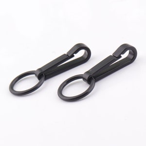Könnte beinhalten: Zwei schwarze Drehclips aus Kunststoff mit einem Metallring. Die Clips sind zum Befestigen an einem Gürtel oder einer Tasche gedacht.