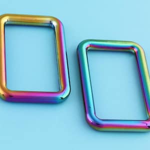 May include: Two iridescent metal D-rings, one slightly larger than the other, with a rainbow finish. The rings are on a light blue background.