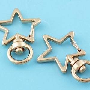 May include: Two gold-toned star-shaped keyrings with swivel clasps. Each keyring has a round metal ring attached to the bottom.
