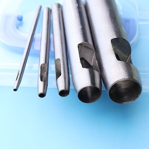 May include: Set of five metal hole punch tools, including a small awl, on a blue background. The tools are used for punching holes in leather, fabric, or other materials.