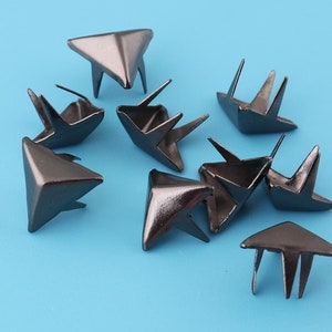 May include: Ten black metal pyramid-shaped studs with three points on each side. The studs have a pointed tip and a flat base.