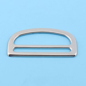 Puede incluir: Una hebilla de metal plateada en forma de D con un acabado liso. La hebilla tiene una abertura rectangular y una parte superior redondeada.