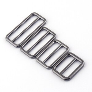 May include: Set of four silver-toned metal slider buckles in various sizes. The buckles are rectangular with a smooth finish.