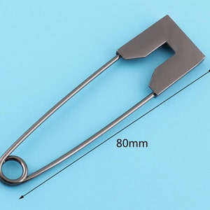 Peut inclure: Une &eacute;pingle &agrave; nourrice argent&eacute;e avec une grande t&ecirc;te rectangulaire. L'&eacute;pingle mesure 80 mm de long.