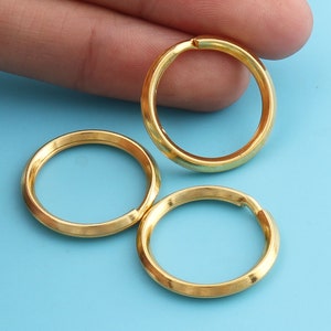 May include: Three gold-colored key rings are displayed against a light blue background. The rings are circular with a small opening, suggesting they are designed to hold keys or other small items. The rings have a smooth, metallic finish.