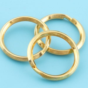 May include: Three gold-colored key rings interlocked against a light blue background. The rings are circular with a smooth, metallic finish. The key rings are designed to hold keys or other small items.