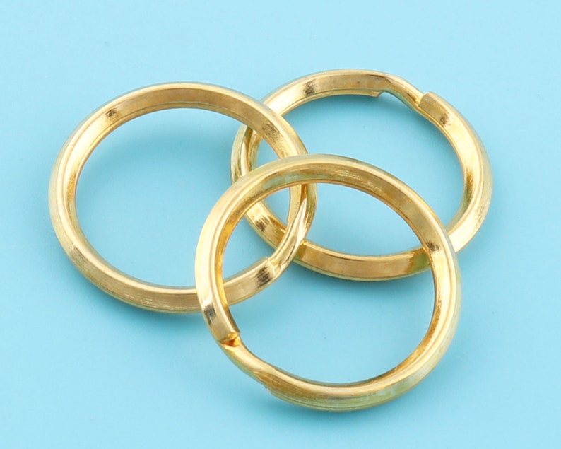 May include: Three gold-colored key rings interlocked against a light blue background. The rings are circular with a smooth, metallic finish. The key rings are designed to hold keys or other small items.