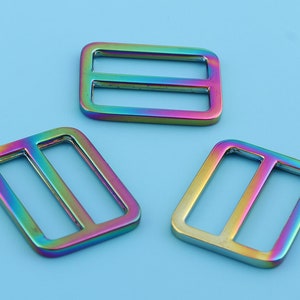 May include: Three iridescent metal slider buckles. The buckles are rectangular with a single horizontal bar in the center. The buckles are a rainbow of colors, including red, orange, yellow, green, blue, and purple.