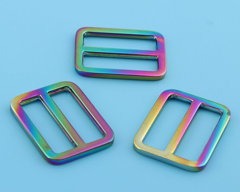 May include: Three iridescent metal slider buckles. The buckles are rectangular with a single horizontal bar in the center. The buckles are a rainbow of colors, including red, orange, yellow, green, blue, and purple.