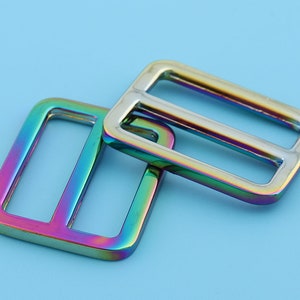 May include: Two iridescent metal slider buckles. The buckles are rectangular with a rounded edge and have a rainbow finish.