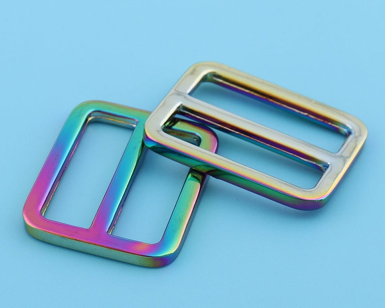 May include: Two iridescent metal slider buckles. The buckles are rectangular with a rounded edge and have a rainbow finish.