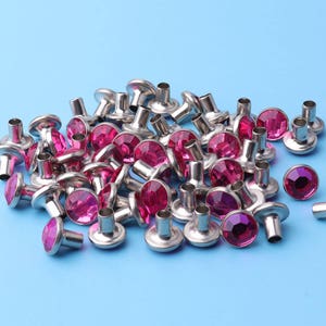 May include: A pile of silver metal studs with pink rhinestones. The studs have a flat base and a round top with a raised rhinestone.