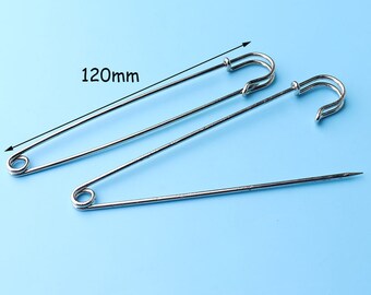 May include: Two silver safety pins, one is 120mm long, the other is shorter. Both are on a light blue background.