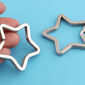 Può includere: Due portachiavi a forma di stella argentati. I portachiavi sono in metallo e hanno una finitura liscia e lucida.