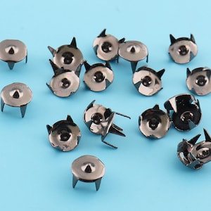 May include: A collection of black metal studs with a pointed tip and a round base. The studs are scattered on a light blue surface.