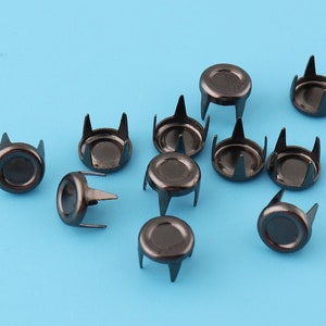 May include: A close-up of a group of black metal studs with four prongs each. The studs are arranged in a random pattern on a blue background.
