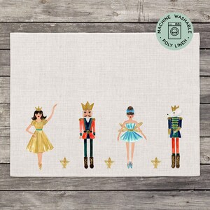 May include: A white linen placemat with a gold, blue, and red illustration of a ballerina, a nutcracker, and a mouse. The placemat has the text "Machine Washable Poly Linen" in a green circle in the top right corner.