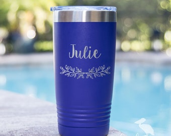 May include: A blue stainless steel tumbler with a white engraved design. The design includes the name "Julie" and a decorative leaf branch.