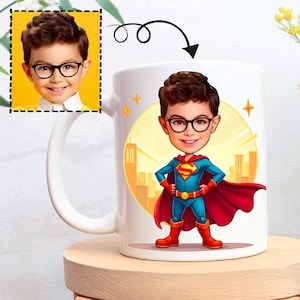 Op de afbeelding: Witte keramische mok met een cartoonillustratie van een jongen in een Superman-kostuum. De jongen draagt een bril en een rode cape. De achtergrond toont een stadsgezicht en gele sterren.