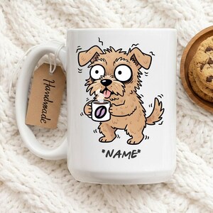 Op de afbeelding: Witte keramische mok met een cartoon hond ontwerp, met een koffiekopje met een koffieboon logo. De mok heeft de tekst "*NAME*" onderaan. Een bruin label met de tekst "Handmade" is aan het handvat bevestigd.