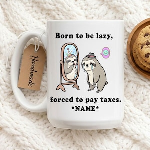 Pode incluir: Caneca de cerâmica branca com um design de bicho-preguiça engraçado. A caneca apresenta o texto "Born to be lazy, forced to pay taxes. *NAME*". Uma preguiça é retratada num espelho e outra a chorar. Uma etiqueta "Handmade" está anexada.