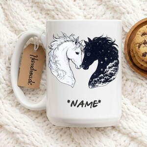 Pode incluir: Caneca de cerâmica branca com uma ilustração a preto e branco de dois cavalos a tocar com os narizes. Um cavalo é branco, o outro é preto com um desenho de céu estrelado. A palavra "*NAME*" está por baixo. Uma etiqueta "Handmade" pende da asa.