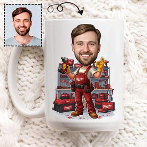 Puede incluir: Taza de cerámica blanca con una ilustración de dibujos animados de un hombre sonriente con un mono rojo sosteniendo un taladro y haciendo el gesto de «ok». El fondo muestra un estante de herramientas y cajas de herramientas, todo en rojo y negro.