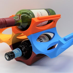 Può includere: Un portabottiglie in plastica colorato a più livelli. Il portabottiglie è arancione, rosso e blu. Contiene due bottiglie di vino.