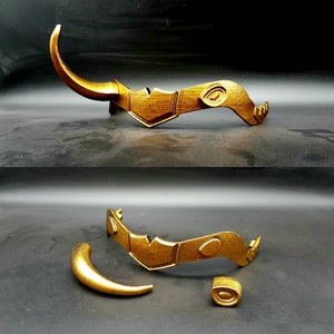 May include: A gold-colored crown with a horn-like design. The crown is in two pieces, with the horn separate from the main crown piece.
