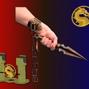 Op de afbeelding: Een gouden ketting met een dolk aan het ene uiteinde. De ketting is bevestigd aan een gouden polsband met een drakensymbool. De dolk heeft een zwart lemmet met een gekartelde rand. Het drakensymbool bevindt zich ook op een aparte gouden cirkel.