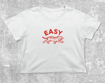 May include: White crop top with a red graphic of a tiger and the word "EASY" above it. The tiger is in a running pose with stripes. The shirt has a crew neck and short sleeves.