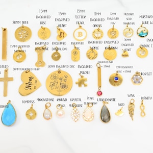 May include: A collection of gold-colored pendants and charms, including crosses, hearts, and discs, with various engraved designs and gemstone accents. Sizes range from 12mm to 40mm. The charms feature a variety of shapes and themes.