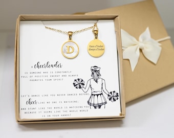 May include: A gold necklace with a round pendant featuring the letter "D" and a second pendant with the text "Once a Trucker Always a Trucker". The necklace is in a gift box with a white ribbon and a card that reads "A cheerleader is someone who is constantly full of positive energy and always promotes team spirit. Let's dance like you never danced before. Cheer like no one is watching. And stunt like the world is watching you because it seems like the whole world is on your hands!"