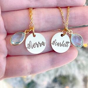 May include: Two gold necklaces with delicate chains and round pendants. The pendants are engraved with the names "Sierra" and "Scarlett" and each has a light blue teardrop-shaped charm.