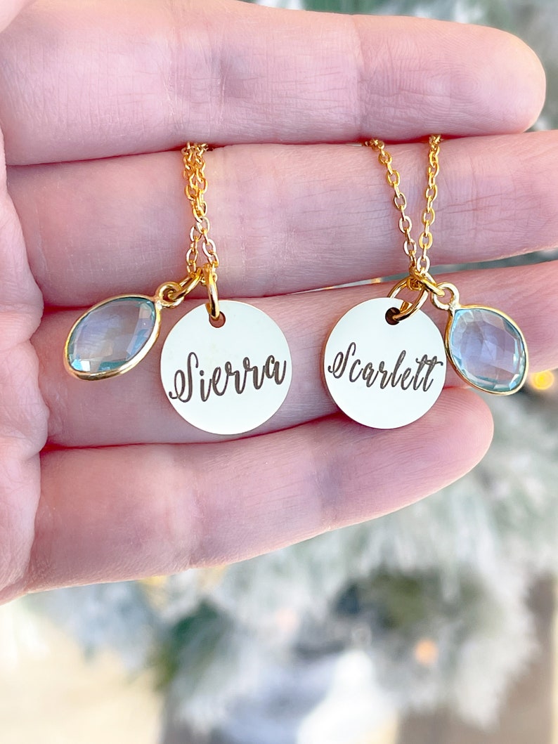 May include: Two gold necklaces with delicate chains and round pendants. The pendants are engraved with the names "Sierra" and "Scarlett" and each has a light blue teardrop-shaped charm.