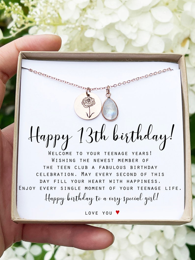 May include: A rose gold necklace with a round pendant featuring a floral design and a teardrop-shaped gemstone. The necklace is presented in a gift box with the text "Happy 13th birthday!" and a birthday message.
